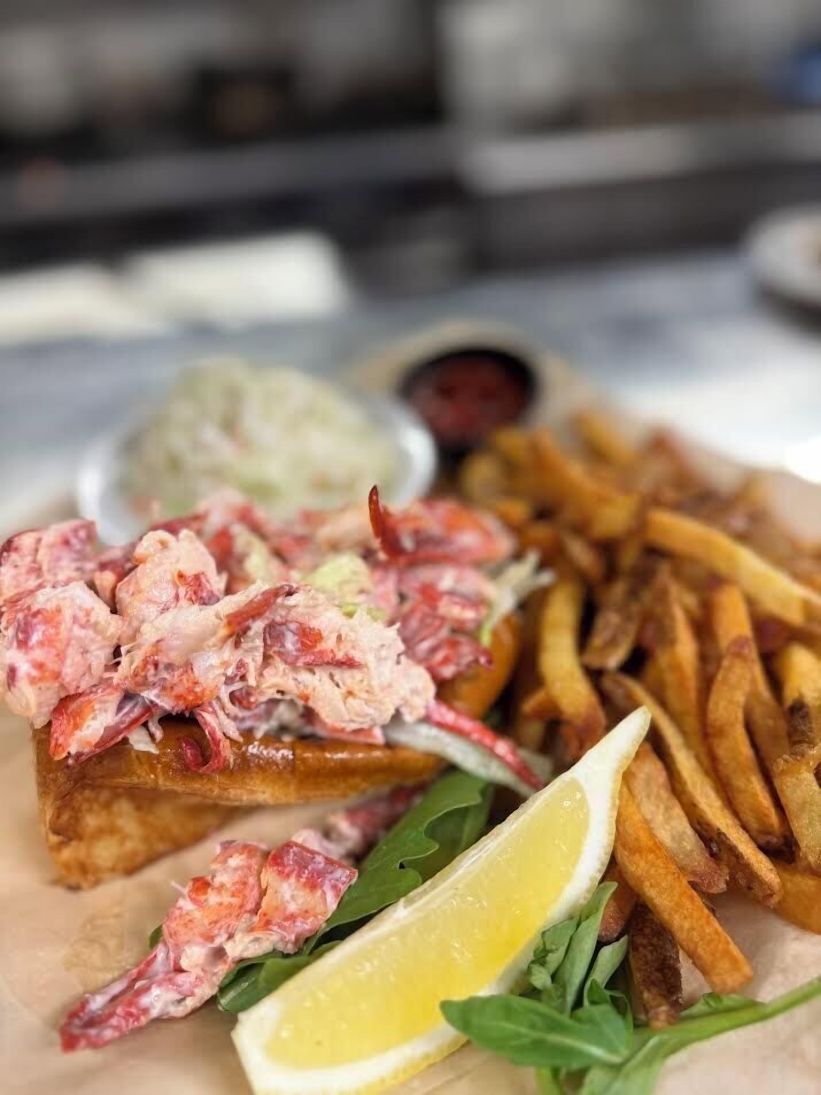 Une assiette de nourriture comprenant du homard, des frites et une tranche de pain accompagnée d’une tranche de citron.