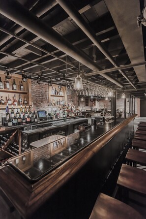 Un bar avec un long comptoir, des étagères remplies de bouteilles et des lampes suspendues.