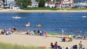 Una playa con gente en balsas y en el agua, una orilla arenosa y casas al fondo.