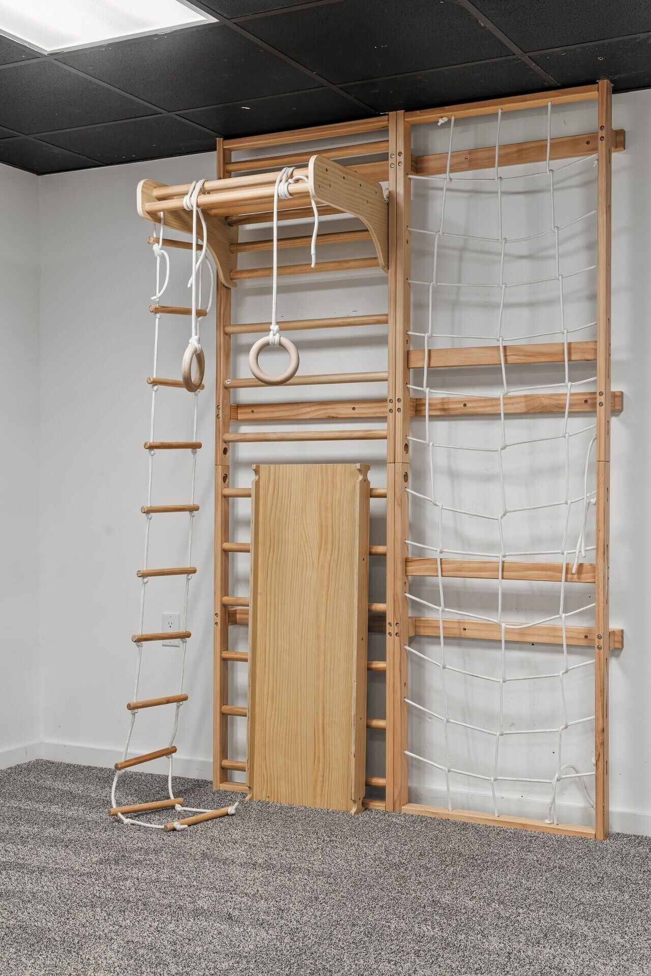 A room with a wooden climbing wall, a netted climbing area, and a door.