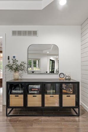 A modern interior with a black and wood console, a large mirror, and a potted plant.