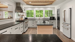 A modern kitchen with white cabinetry, a central island, a built-in oven, and a stainless steel range hood. - Woodland Retreat at Fair Hill- Hot Tub, Pool, and Sport Court (Elkton)