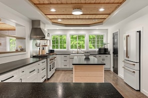 A modern kitchen with white cabinetry, a central island, a built-in oven, and a stainless steel range hood.