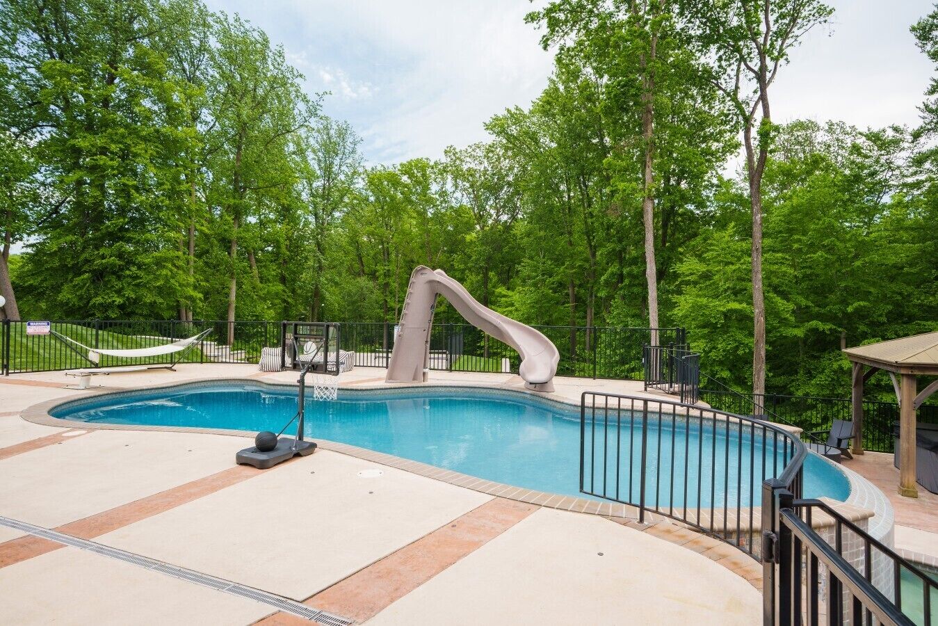 Une piscine avec un toboggan, entourée d’une clôture et d’arbres.