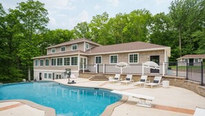 A large house with a swimming pool, outdoor seating, and a fenced patio area. - Woodland Retreat at Fair Hill- Hot Tub, Pool, and Sport Court (Elkton)