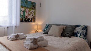 A neatly made bed with towels, a painting on the wall, and a nightstand with a lamp. - Almyrà House_ Costa dei Trabocchi (Abruzzo)