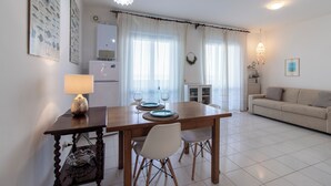 A dining area with a wooden table, white chairs, and a lamp. There is a kitchen in the background with a refrigerator and a microwave. - Almyrà House_ Costa dei Trabocchi (Abruzzo)