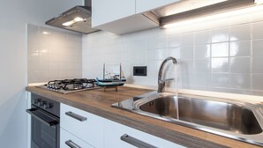 A modern kitchen with white cabinets, a stainless steel sink, a wooden countertop, and a gas stove. - Almyrà House_ Costa dei Trabocchi (Abruzzo)