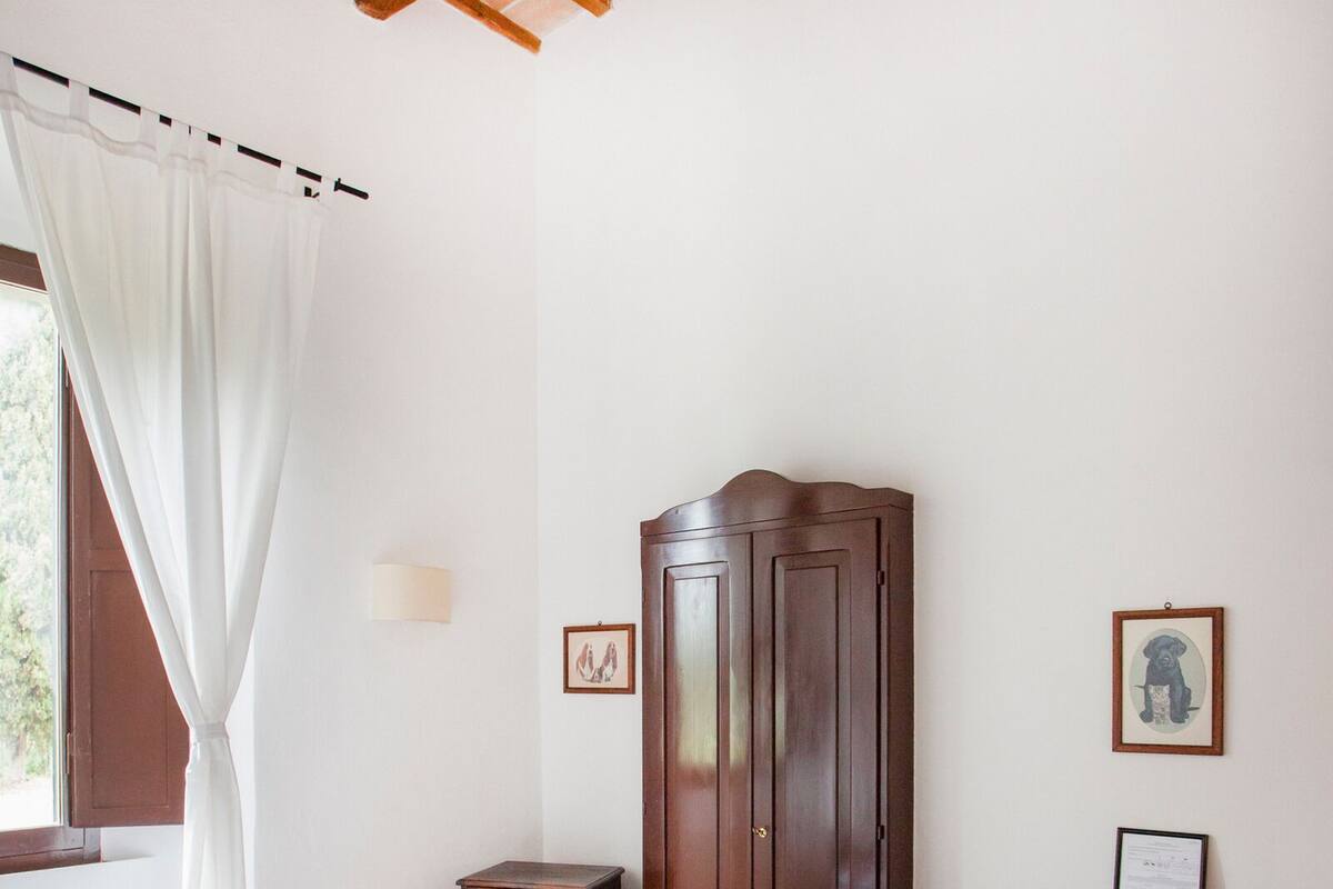 Een slaapkamer met een bed, een houten kledingkast, een bureau en een raam met gordijnen.