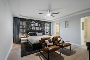 Ein modernes Schlafzimmer mit einem Bett, zwei Ledersesseln, einem Deckenventilator und einer Wand mit Steinmuster.