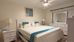 Een slaapkamer met een bed, nachtkastjes, een plafondventilator, een schilderij, een spiegel en een dressoir.