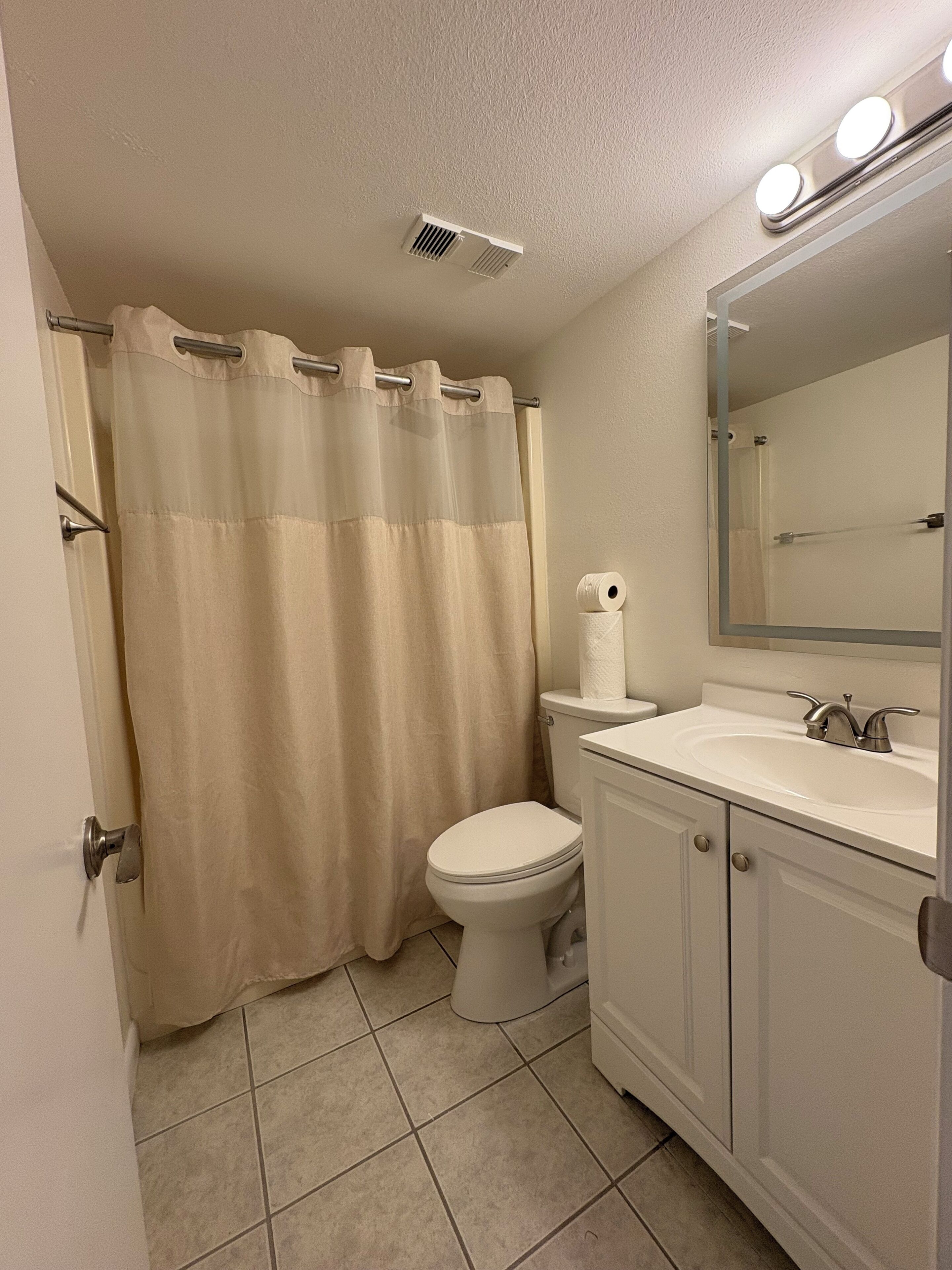 A bathroom with a toilet, sink, mirror, and shower curtain.