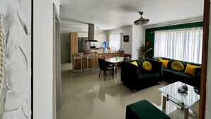 Een moderne woonkamer met een groene bank, een salontafel en een eethoek met een keuken op de achtergrond.