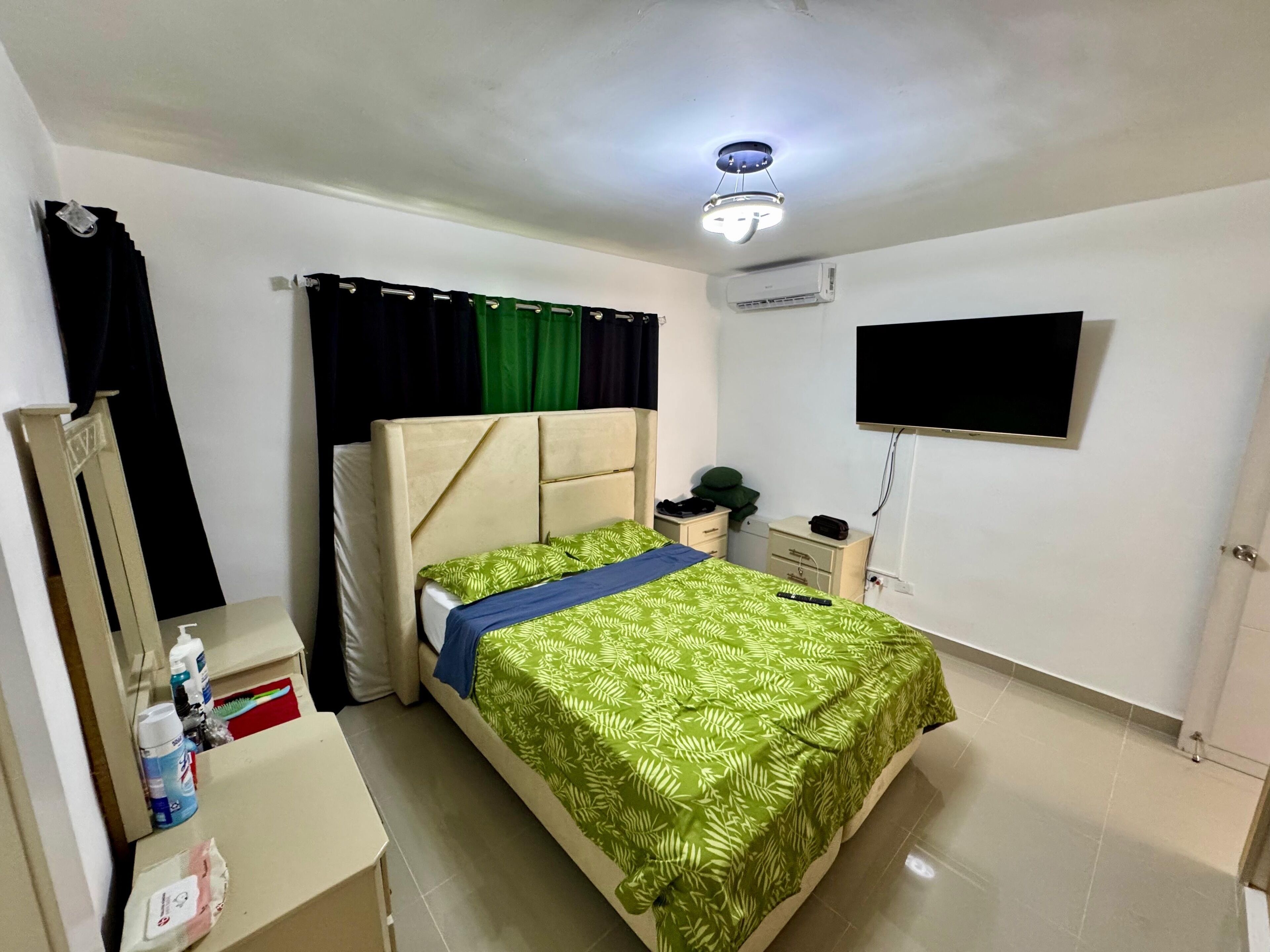 A bedroom with a bed, bedside table, mirror, and a TV mounted on the wall.