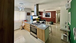 Een moderne keuken met een centraal eiland, roestvrijstalen apparatuur en een eetgedeelte met een groene accentmuur.