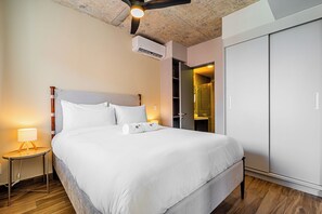 Una habitación de hotel con una cama grande, una lámpara de noche, un equipo de aire acondicionado y un armario.