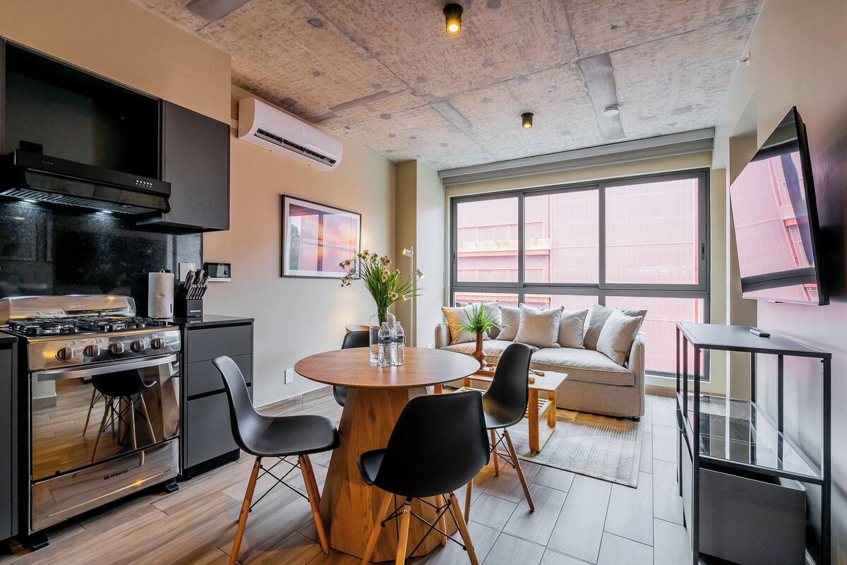 Una cocina moderna con estufa, mesa de comedor y sillas, sofá y un amplio ventanal con vistas.