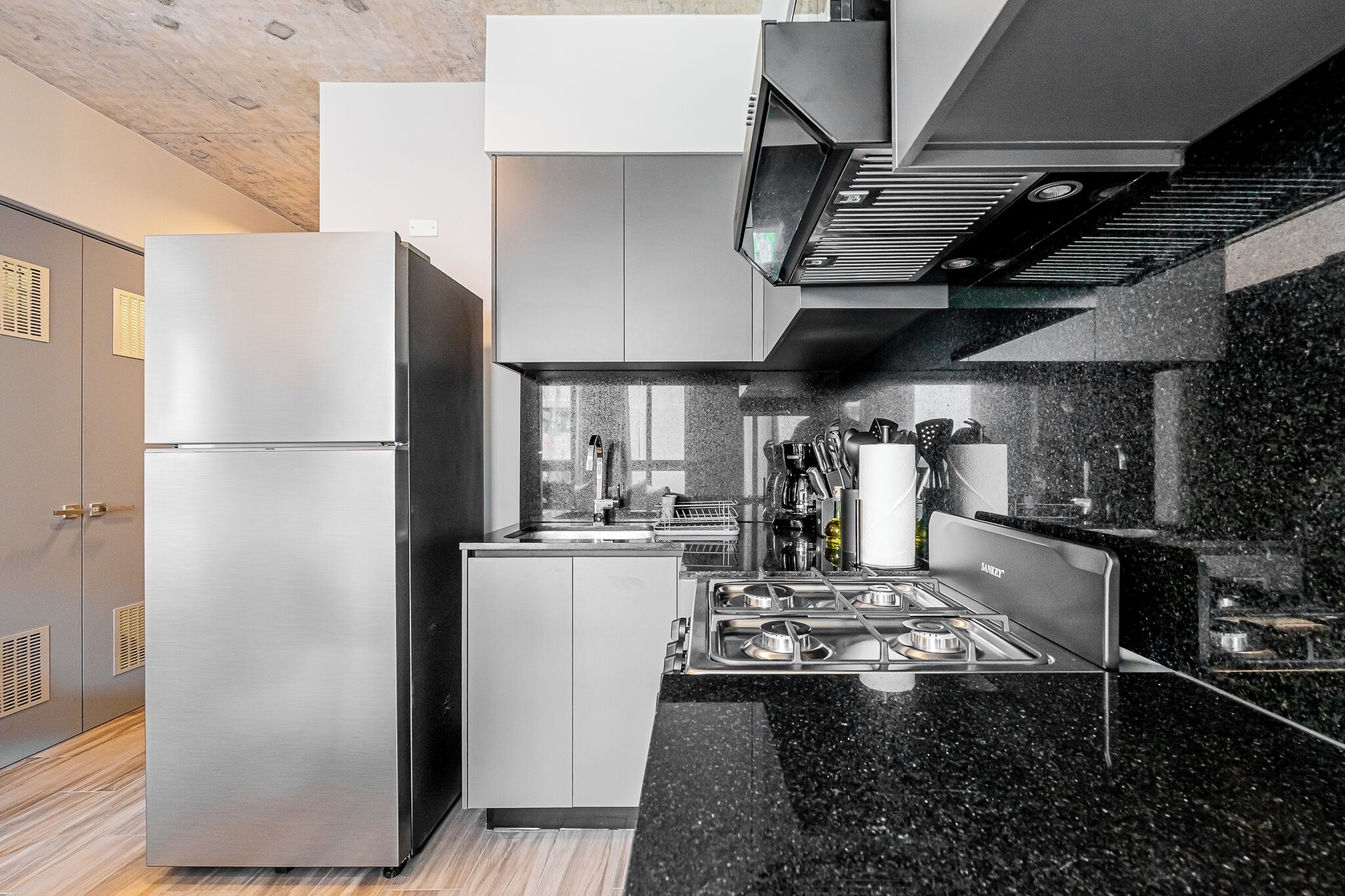 A modern kitchen with a stainless steel refrigerator, a built-in stove, and a black granite countertop.