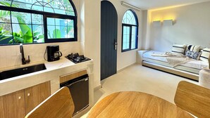 A modern kitchen with a dishwasher, a coffee maker, and a gas stove. There is a dining area with a wooden table and chairs. The room has large windows with a view of greenery outside. - Villa Kalah (Puerto Triunfo)
