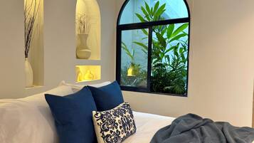 Un dormitorio con cama, almohadas azules estampadas, una manta gris y una ventana con vistas a zonas verdes.