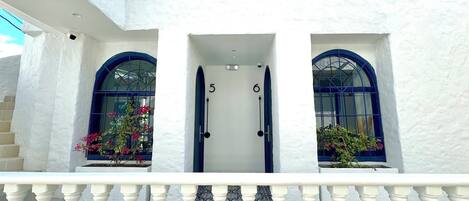A building with a white facade, two arched windows with blue frames, and a balcony with white balustrades.