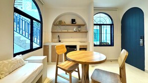 A compact living space with a kitchenette, a dining area with a round table and chairs, and a large window providing a view of the outside. - Villa Kalah (Puerto Triunfo)