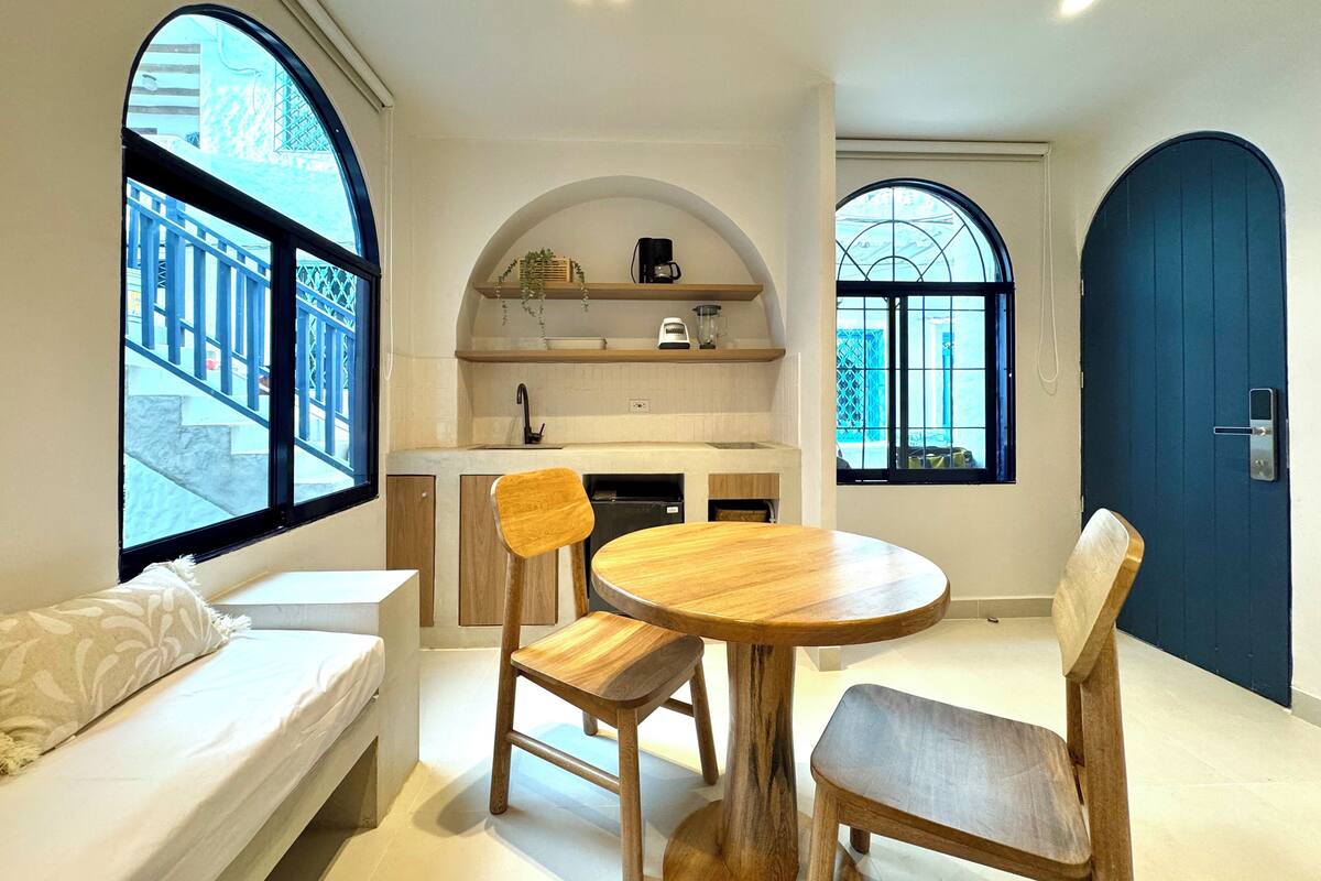 A compact living space with a kitchenette, a dining area with a round table and chairs, and a large window providing a view of the outside.