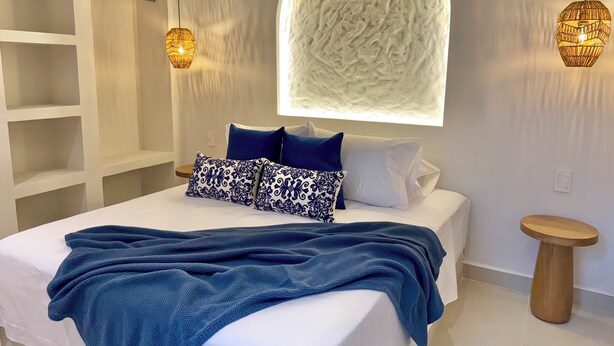 A modern bedroom with a large bed, a unique textured wall feature, and two pendant lights. - Villa Kalah (Puerto Triunfo)