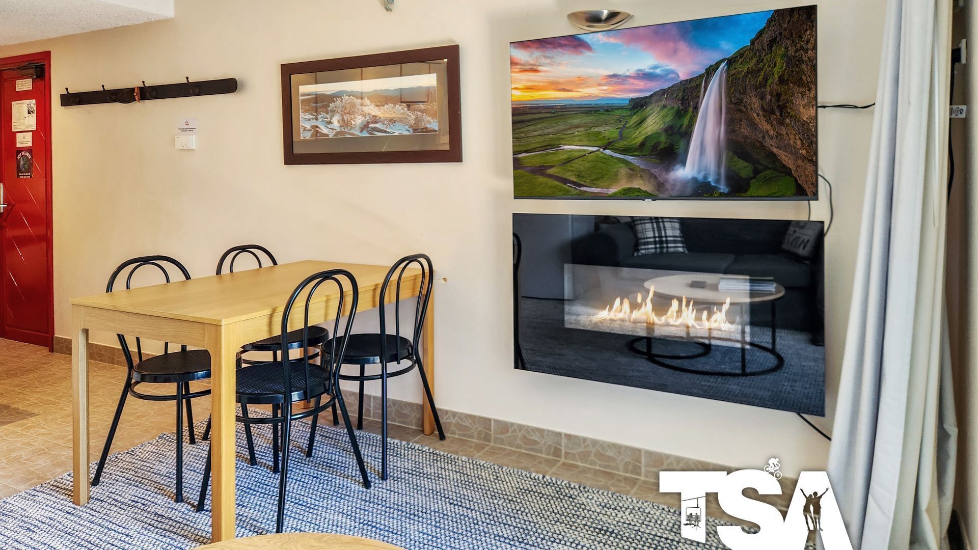 A dining area with a wooden table and black chairs, a fireplace, and two framed pictures on the wall.