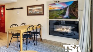A dining area with a wooden table and black chairs, a fireplace, and two framed pictures on the wall. - Sashas 2 - Central Village (Central Village)