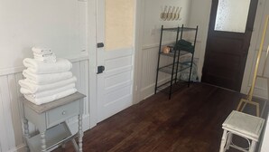 A room with a wooden floor, a white door with a window, a small table with folded towels, and a metal shelf unit with bags.