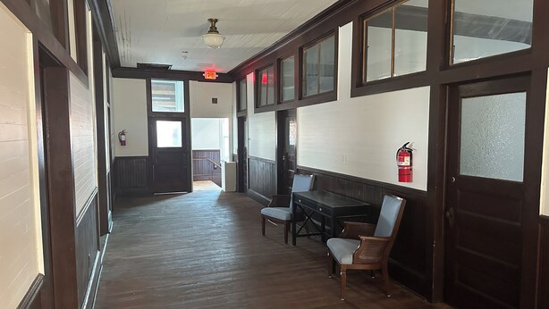 A hallway with wooden flooring, a table with chairs, and a fire extinguisher on the wall.