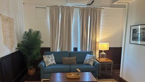 A living room with a blue sofa, a wooden coffee table, a lamp, a macrame wall hanging, and a potted plant.