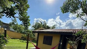 A small yellow building with a tiled roof, a hammock, and a large green leaf in the foreground. - POUSADA PEQUIZEIRO (Chapada dos Guimarães)