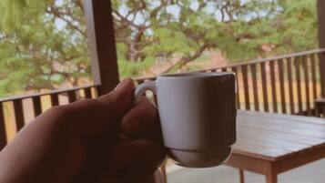 Une main tenant une tasse blanche sur une table en bois, sous un toit recouvert de tuiles.