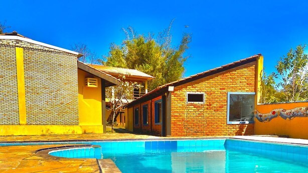 A swimming pool with a stone deck, a small brick building with a window, and a yellow wall. - POUSADA PEQUIZEIRO (Chapada dos Guimarães)