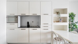 A modern kitchen with white cabinetry, a built-in oven, a coffee maker, and a dining area with a white table and chairs. - GuestReady - Welcoming place in Porto (Boavista)