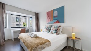A modern hotel room with a large bed, a desk, and a window with a city view. - GuestReady - Welcoming place in Porto (Boavista)