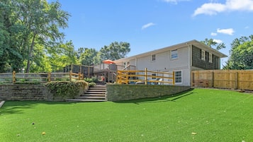 A residential property with a well-maintained lawn, a wooden deck, and a two-story house with a visible staircase.