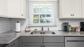 Eine Küche mit weißen Schränken, einer Spüle, einem Fenster mit Jalousien und einer Kaffeemaschine.