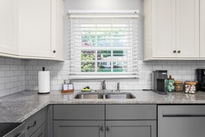 A kitchen with white cabinets, a sink, a window with blinds, and a coffee maker. - Horseshoes, Fire Pit, HOT TUB, Xbox Series S, Grill Outside (Greensboro)