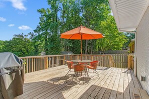 A wooden deck with a table and chairs, an orange umbrella, and a barbecue grill. - Horseshoes, Fire Pit, HOT TUB, Xbox Series S, Grill Outside (Greensboro)