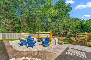 A patio area with a fire pit, blue chairs, and a wooden fence. - Horseshoes, Fire Pit, HOT TUB, Xbox Series S, Grill Outside (Greensboro)