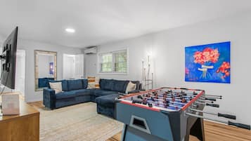 A living room with a foosball table, a blue sofa, a television, and a painting of flowers.