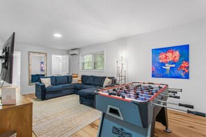 Una sala de estar con mesa de fútbol, un sofá azul, un televisor y un cuadro de flores.