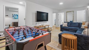 Ein modernes Wohnzimmer mit Tischfußball, einem Flachbildfernseher, einem blauen Sofa und einem Couchtisch aus Holz.