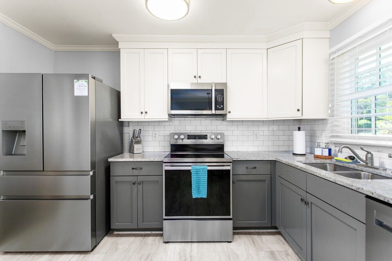 A modern kitchen with stainless steel appliances, white cabinetry, and a window providing natural light.