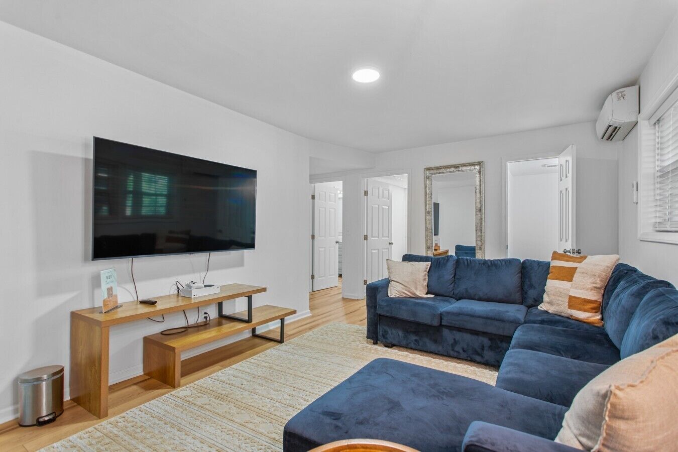 Ett modernt vardagsrum med en platt-TV, en blå soffa, ett träbord och en stor spegel.