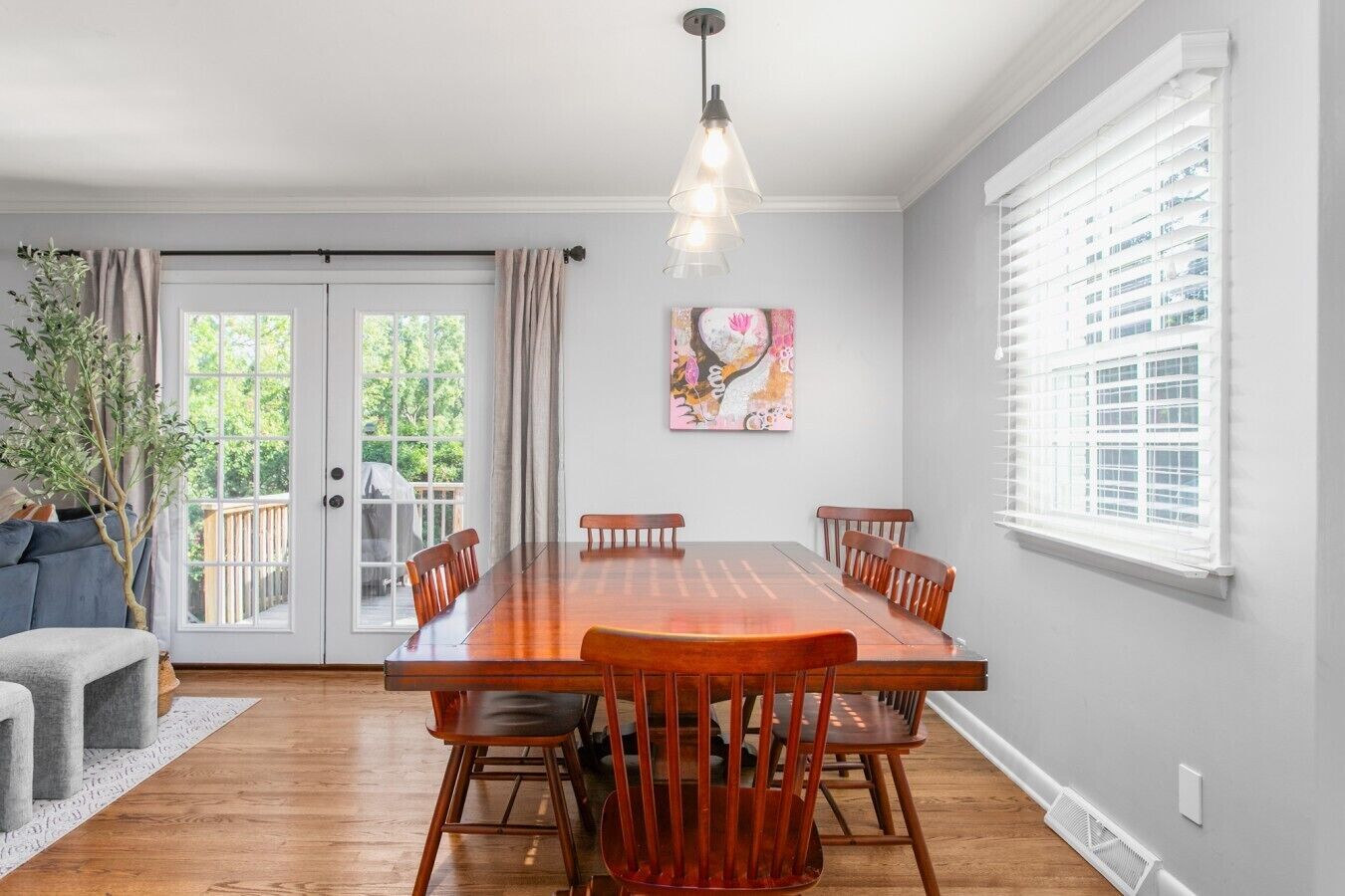 A dining area with a wooden table and chairs, a pendant light, and a painting on the wall.