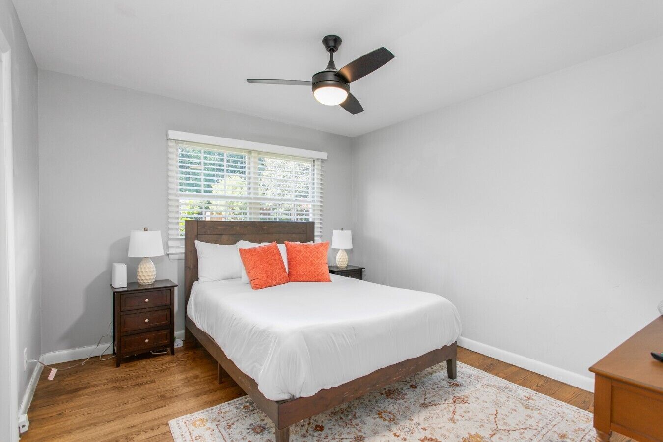 Une chambre à coucher avec un lit, des tables de chevet, un ventilateur de plafond et une fenêtre avec des stores.